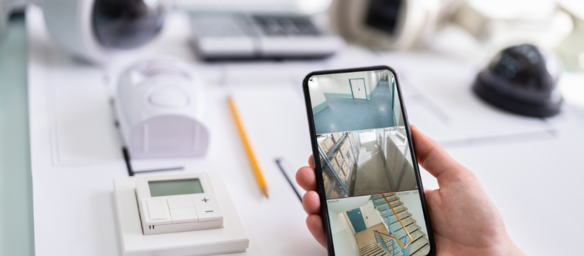 Intruder Alarm System items on a desk and a person holding a mobile phone with 3 different security views showing on the screen